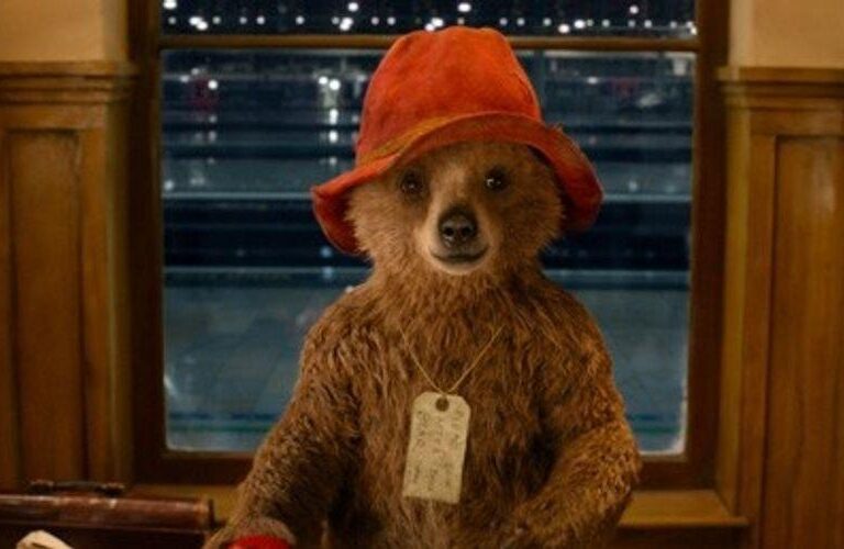 Brown bear in a red hat seated in a wood-paneled restaurant booth, with a tag hanging from its neck.